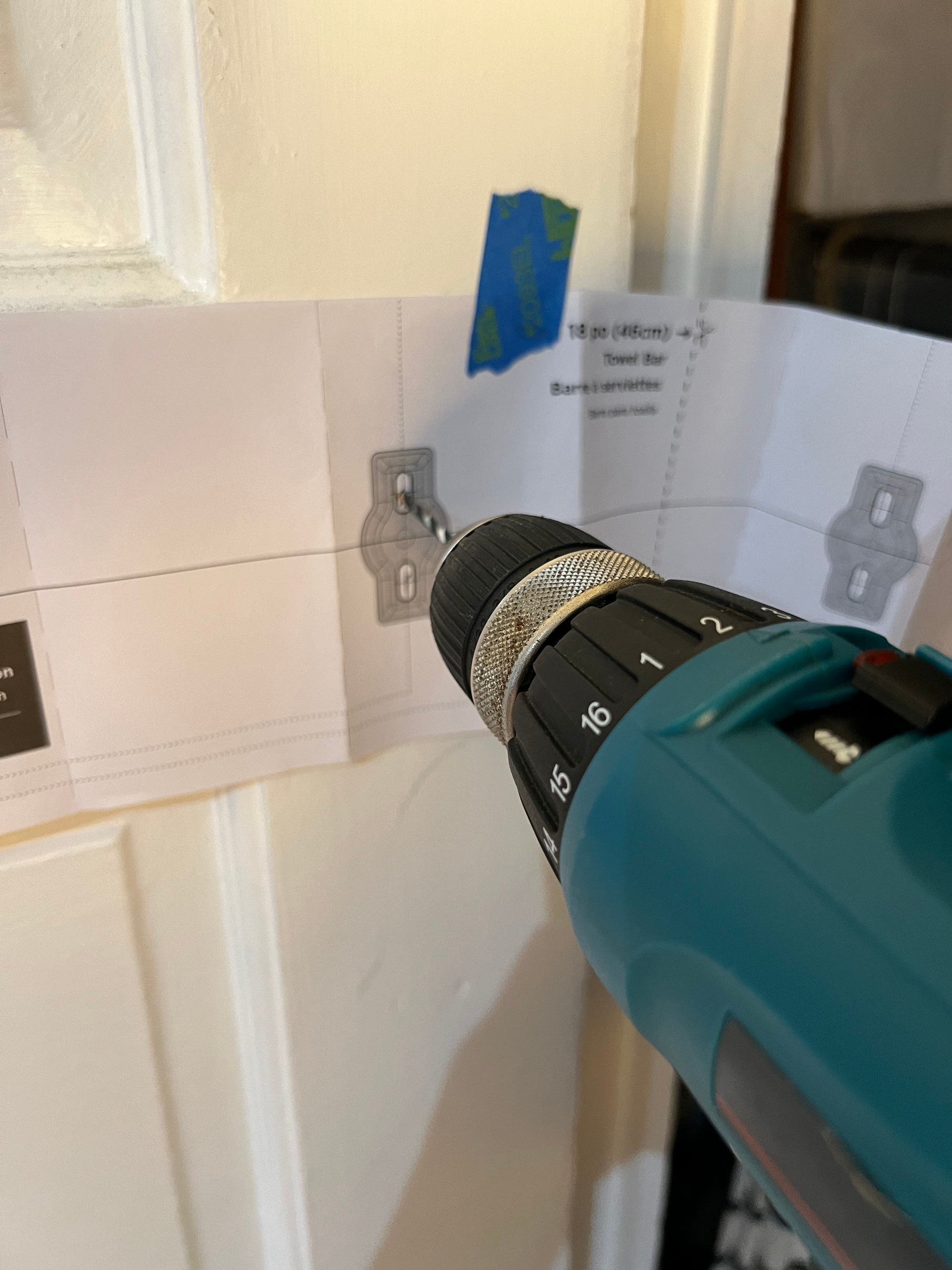 Teal Makita drill with bit in place drilling holes using a paper template for the towel bar DIY small space storage solutions