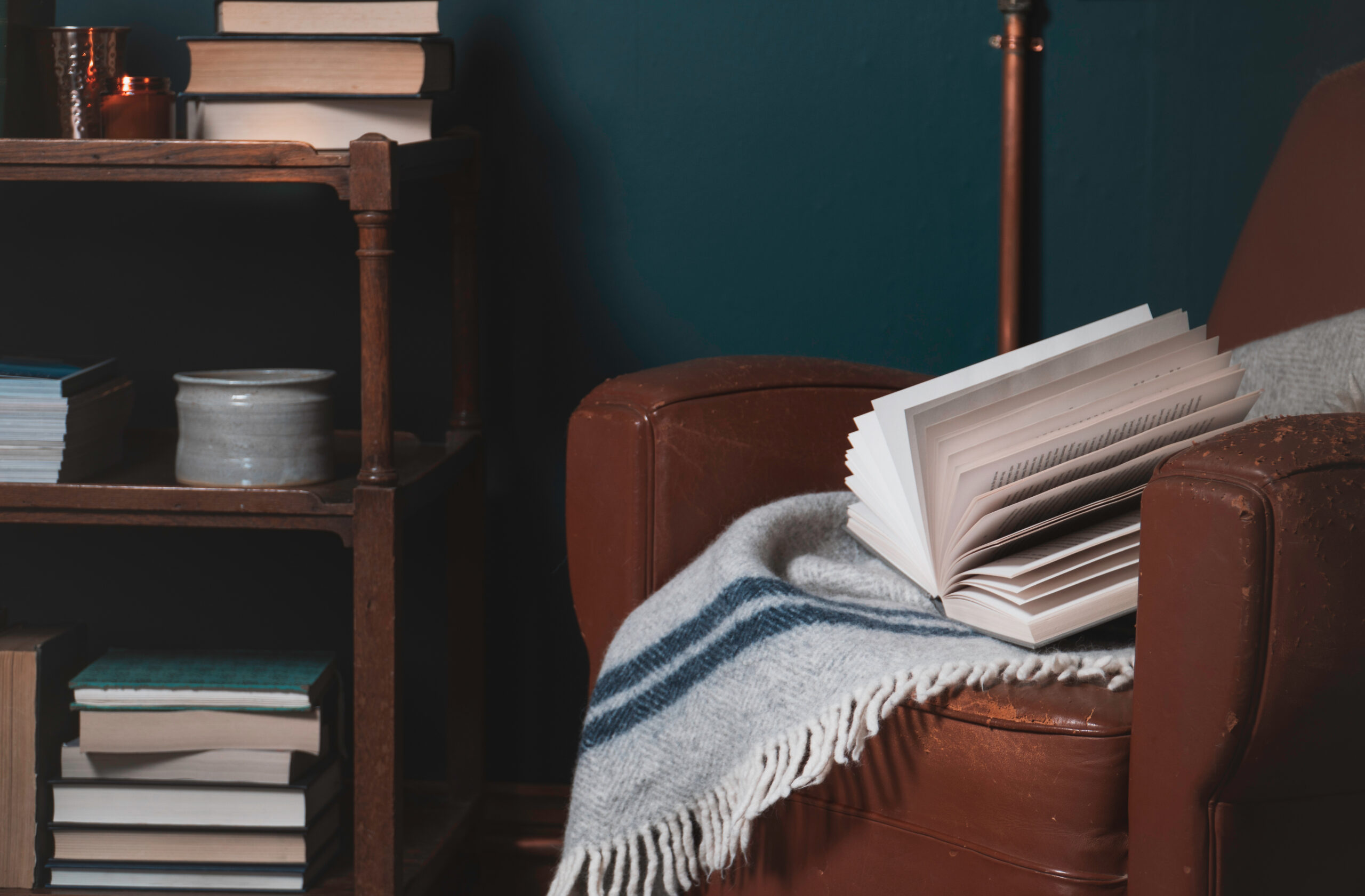 worn brown leather chair, blue wall, bookshelf, books, gray and blue throw blanket decorating tips for small spaces,