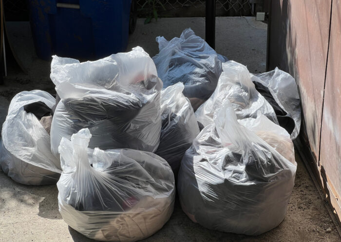 fashion brands destroy unused merchandise Clear bags of fast fashion waste from the alley by a brown metal gate Those Someday Goals