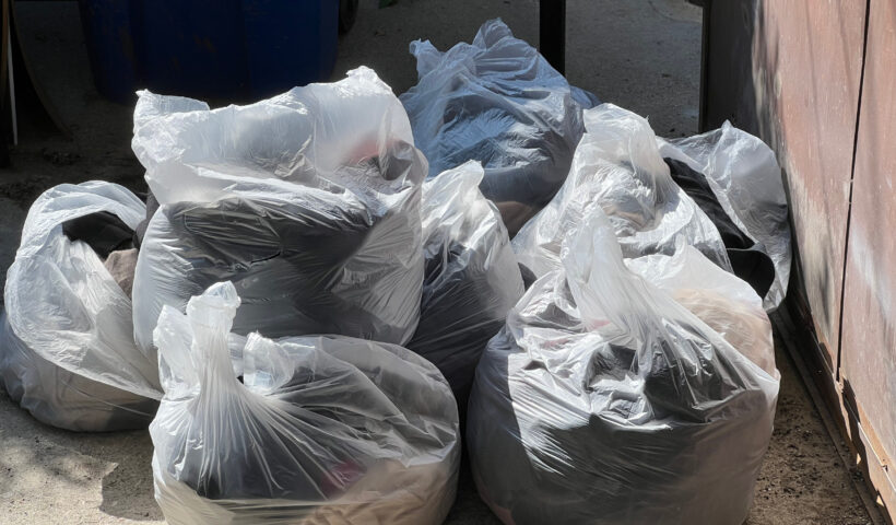 fashion brands destroy unused merchandise Clear bags of fast fashion waste from the alley by a brown metal gate Those Someday Goals