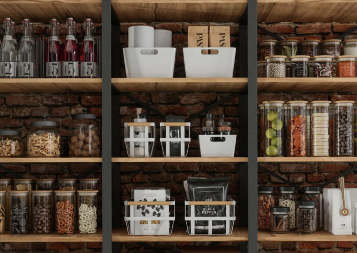 Organized Pantry with clear storage bins and containers with labels against a brick wall Those Someday Goals