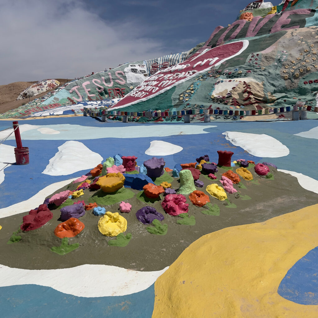 Art by Leonard C Knight Bright flowers and the start of the yellow brick road at Salvation Mountain