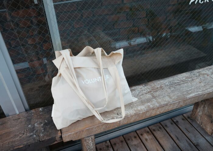 Off-white canvas tote bag with the word Volunteer in white letters sitting on an old wooden bench 30 Bags in 30 Days Those Someday Goals Photo credit: Lex Sirikiat