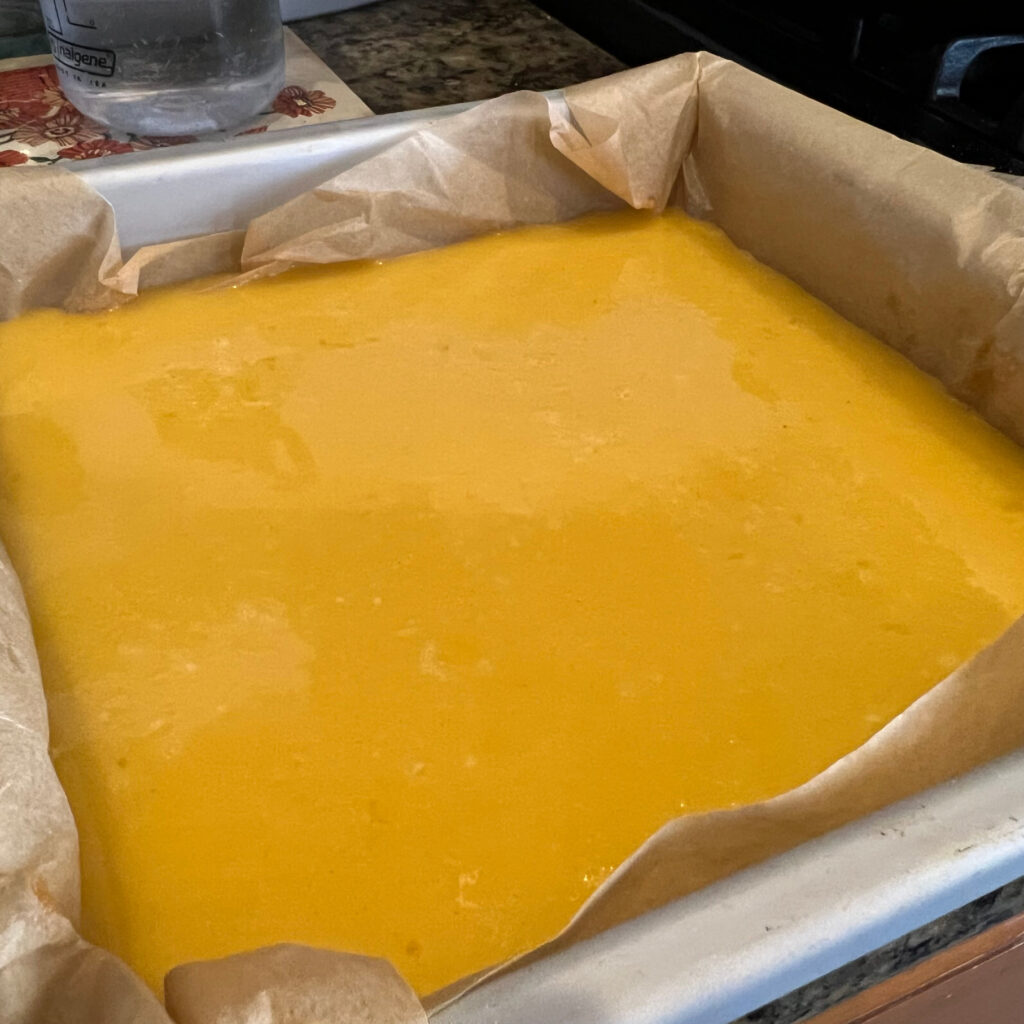 Passion fruit bar mixture on top of shortbread crust surrounded by brown parchment paper in a gray aluminum baking pan Those Someday Goals