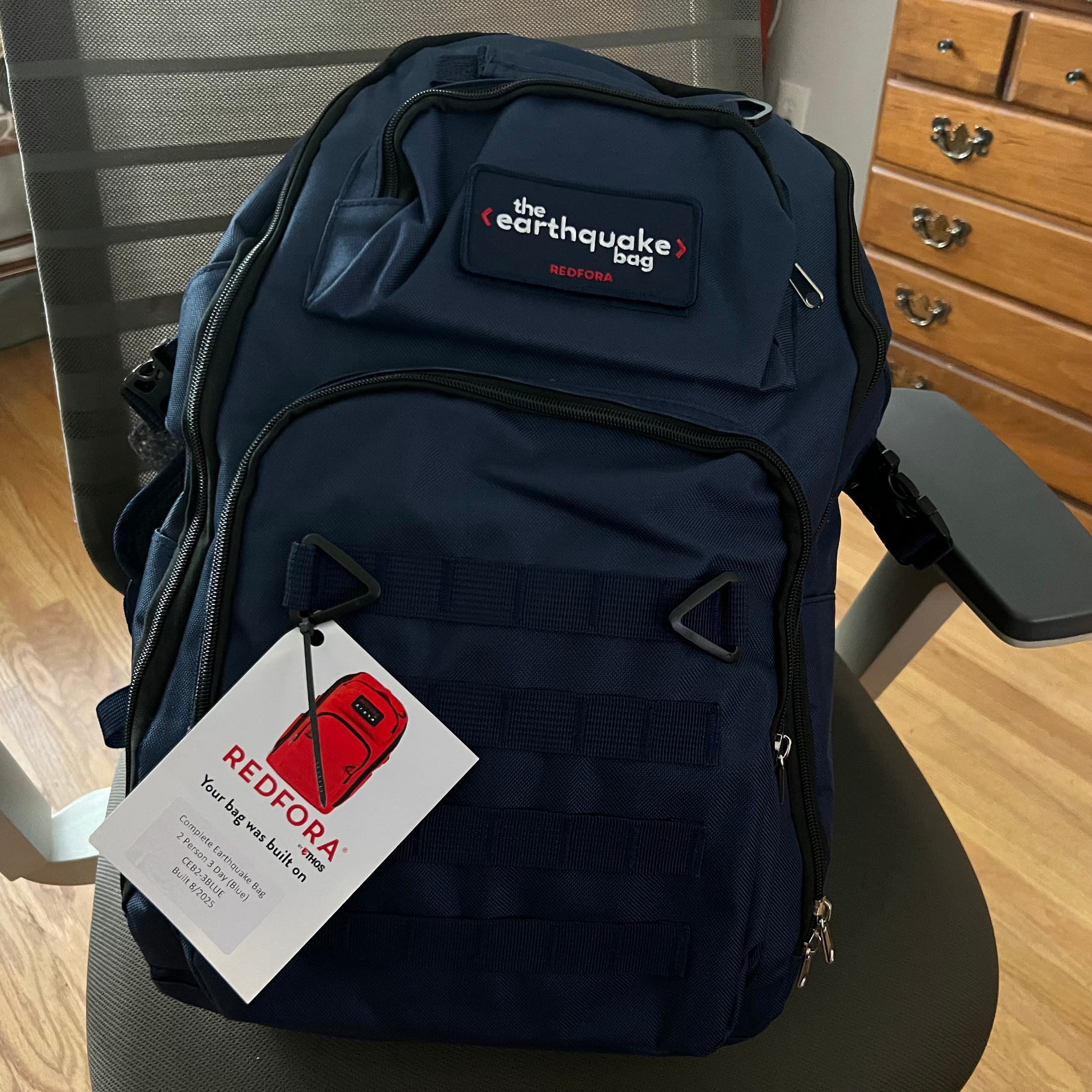 Redfora's Earthquake Bag in blue sitting on a desk chair over a wood floor near a cabinet