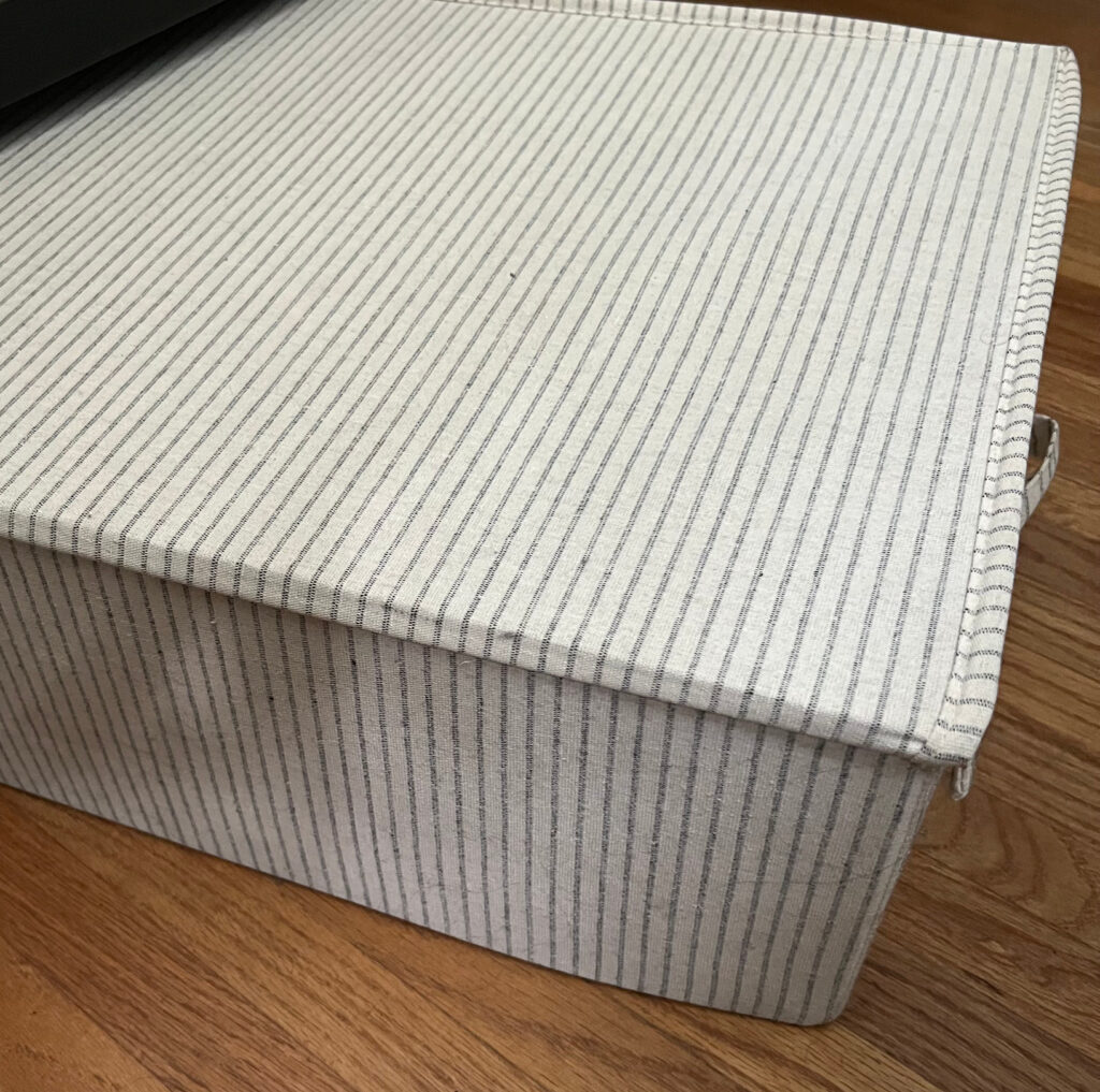 Off-white and gray striped under-bed storage bin against wood floor cozy closet refresh Those Someday Goals